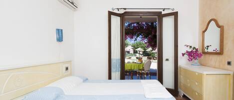 A bedroom with two beds, a dresser, and a view of an outdoor dining area.