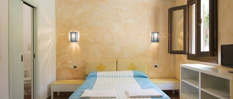Une chambre à coucher avec un lit, des tables de chevet, un banc et un téléviseur posé sur un meuble.
