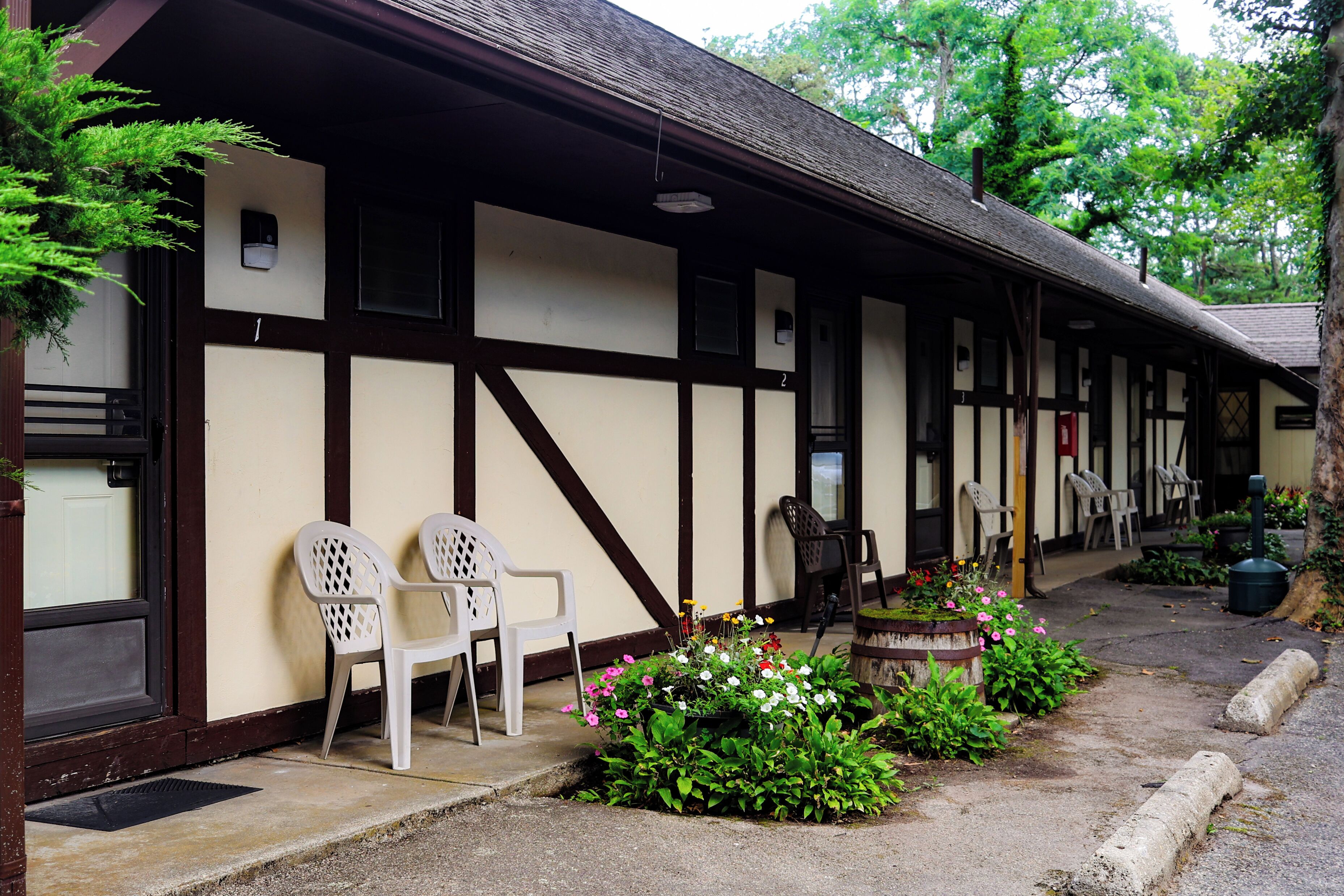 Un bâtiment traditionnel doté d’un porche, de chaises en plastique blanches et d’un parterre de fleurs.
