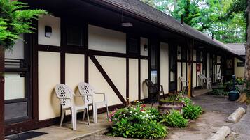 A traditional building with a porch, white plastic chairs, and a flower bed.