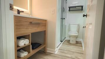 A modern bathroom with a wooden vanity, a glass shower enclosure, and a toilet.