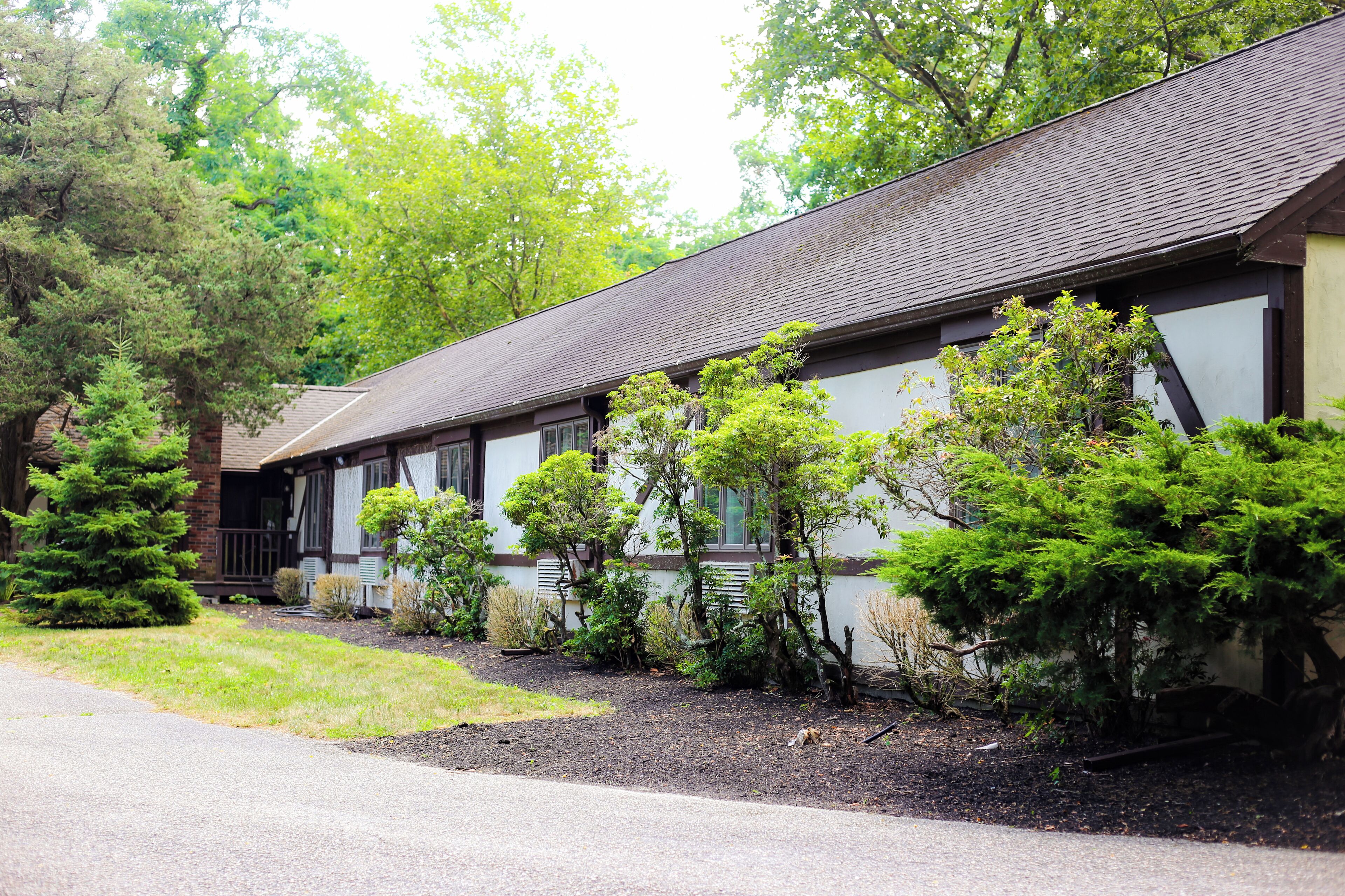 A row of traditional-style buildings with a sloped roof, surrounded by well-maintained landscaping and trees.