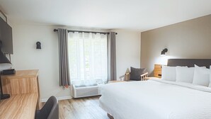 A modern hotel room with a wooden desk, a comfortable chair, a large bed with white bedding, and a window with curtains.