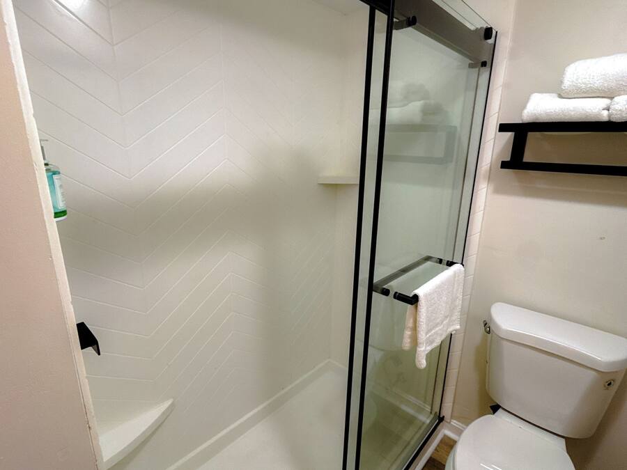 A modern bathroom with a glass-enclosed shower, a white toilet, and a shelf with towels.