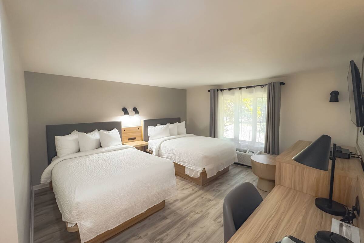 Een hotelkamer met twee bedden, een bureau, een stoel, een televisie en een raam met gordijnen.
