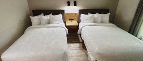 A double room with two beds, a wooden nightstand, and a wall-mounted light fixture.