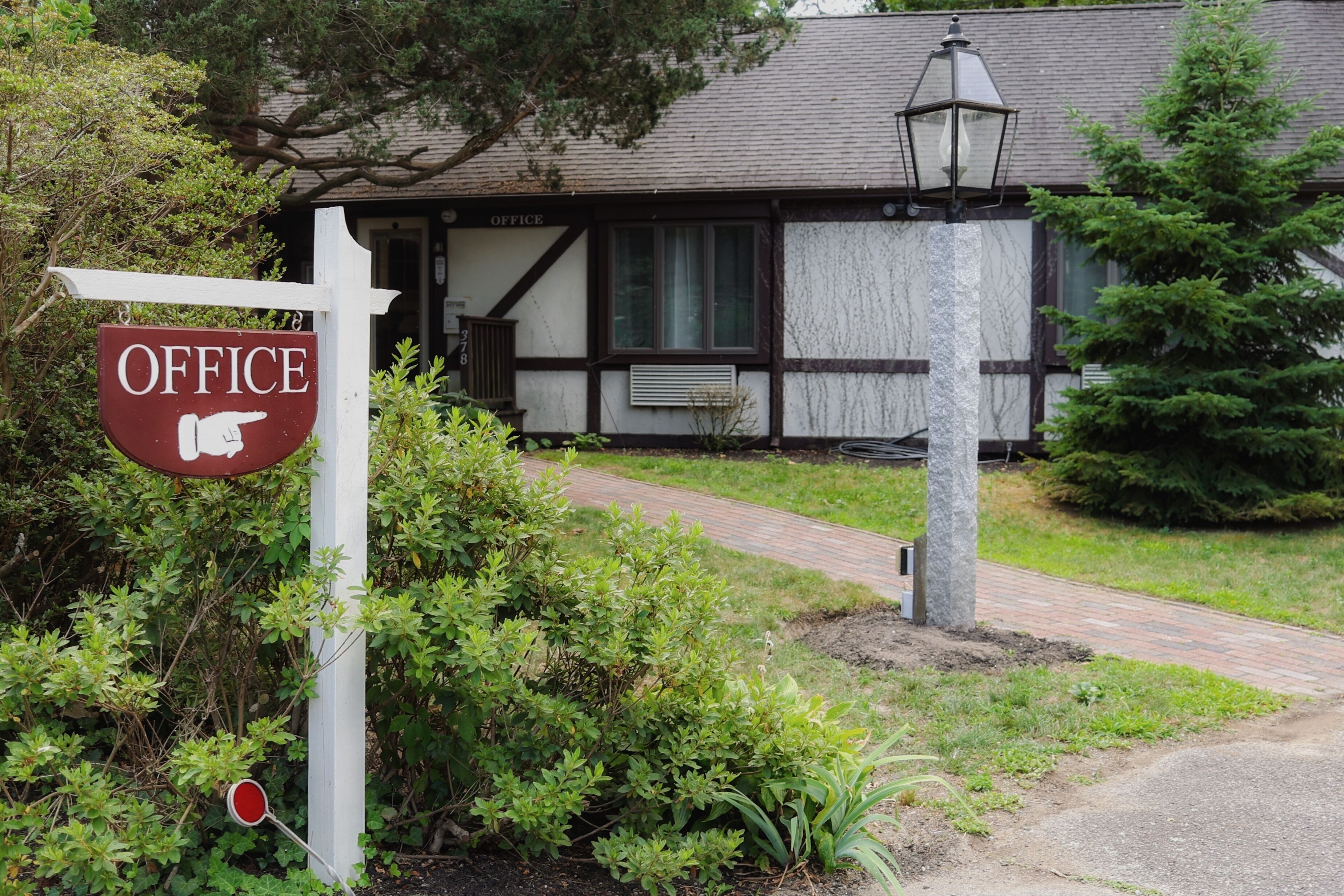A building labeled "OFFICE" with a pointed sign, surrounded by greenery and a brick pathway.
