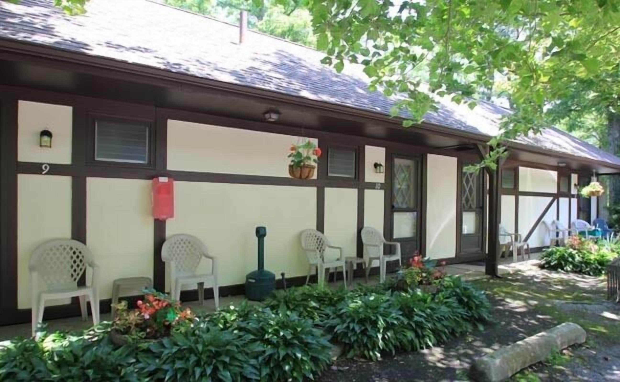 A building with a row of white plastic chairs outside, a red mailbox, and a potted plant on the porch.