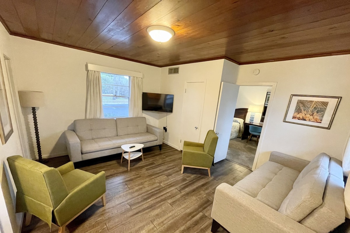 A furnished living room with a sofa, two armchairs, a coffee table, and a television.