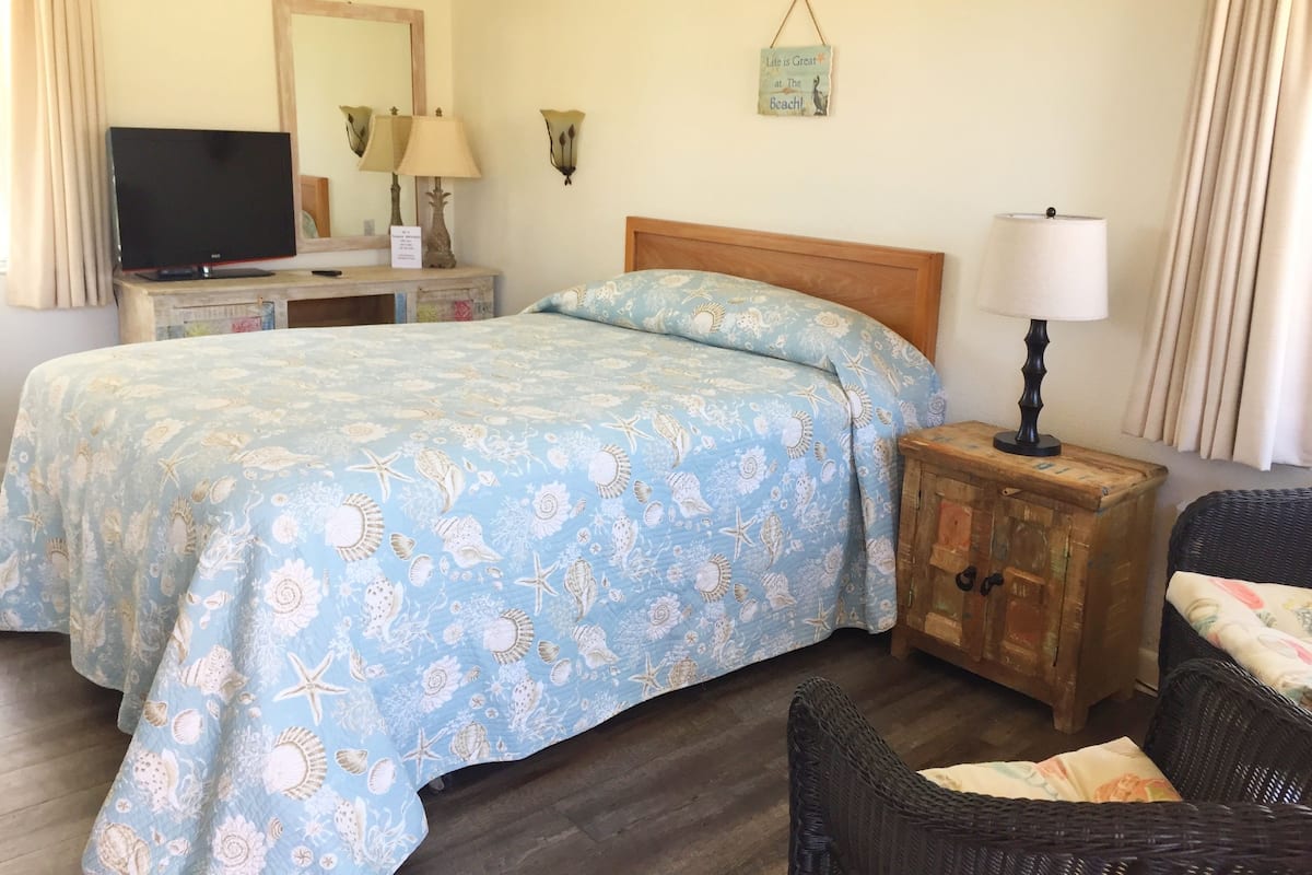 A bedroom with a bed, a television, a nightstand, a lamp, and a wicker chair.