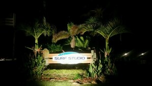 Un panneau en bois sur lequel est écrit « SURF STUDIO », entouré de palmiers et de plantes.