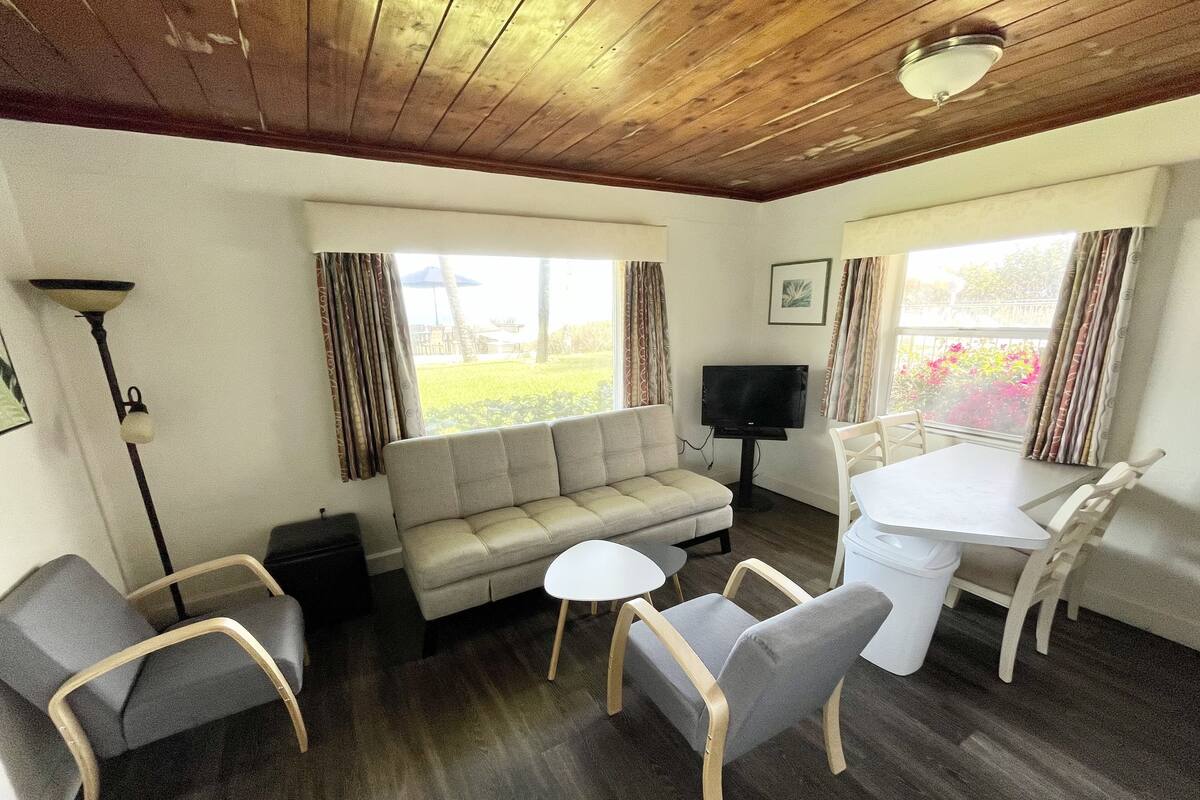 A furnished room with a sofa, two armchairs, a small table, a TV, and a window with curtains.
