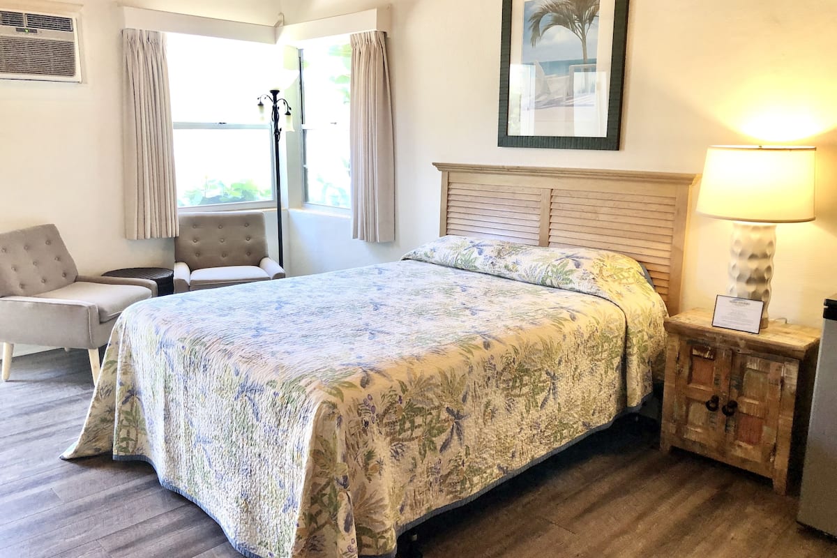 A bedroom with a bed, a chair, a lamp, and a window with curtains.