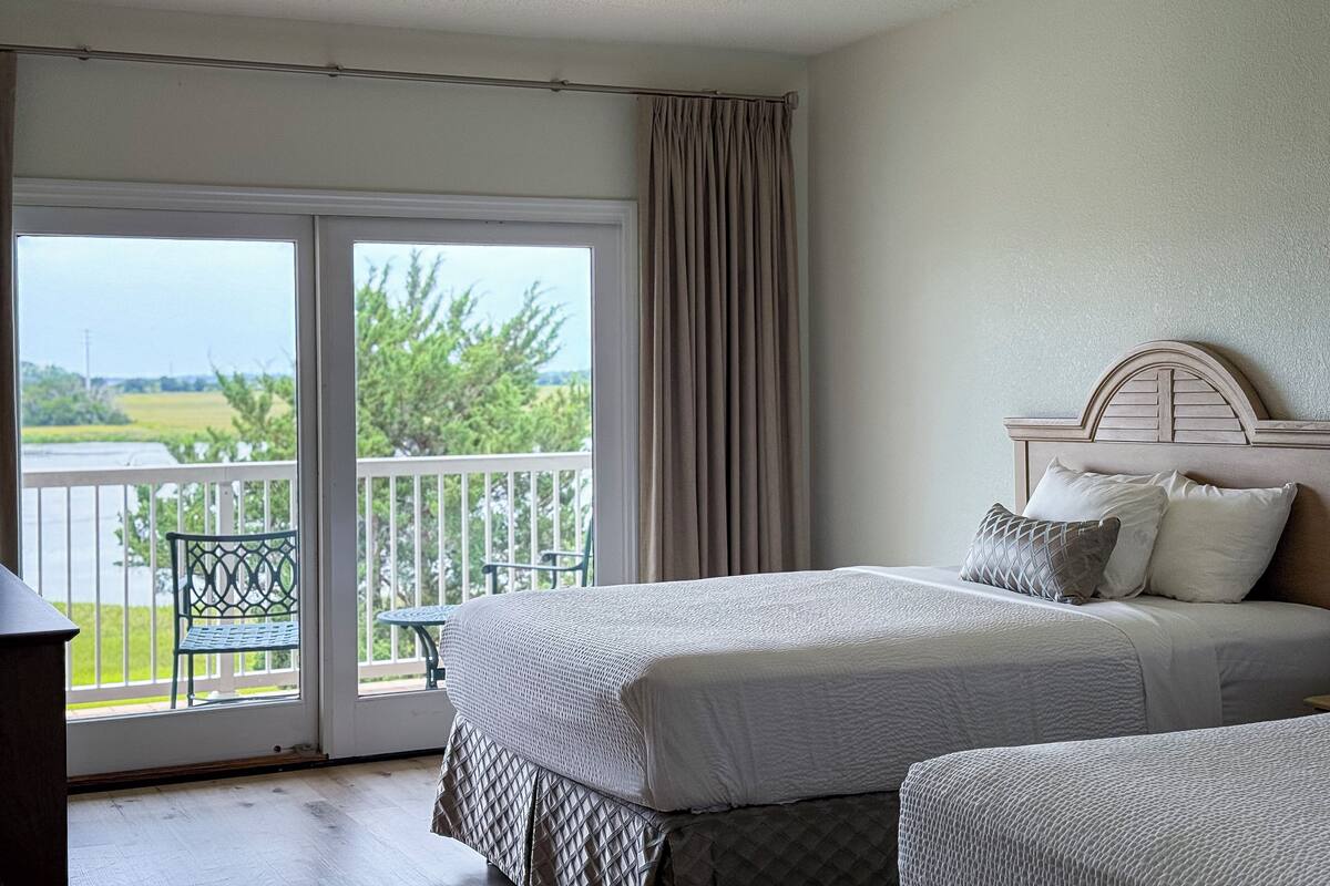 Un dormitorio con cama, vista a un balcón y una silla afuera.