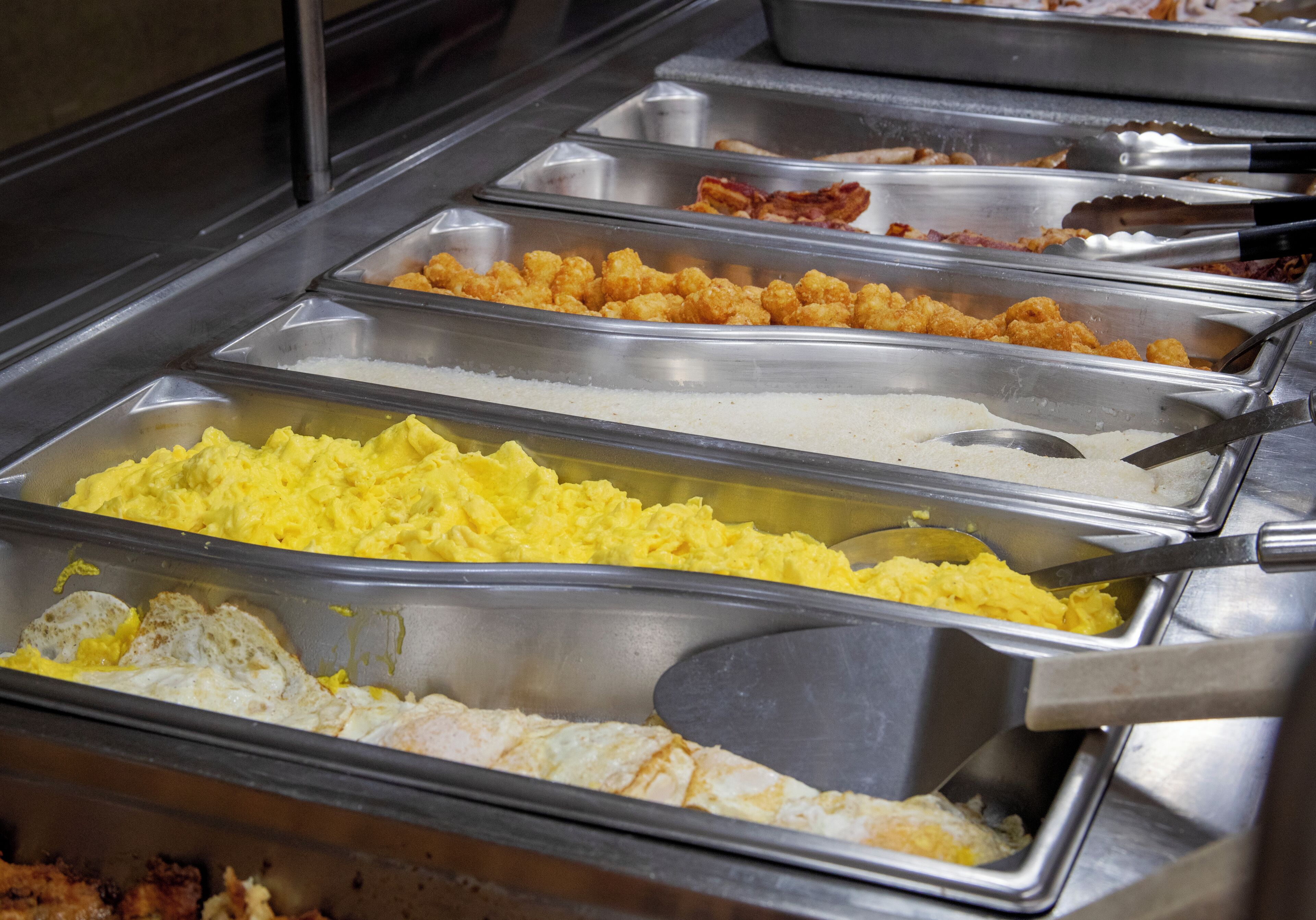 A buffet with various food options including scrambled eggs, fried chicken, and other dishes.