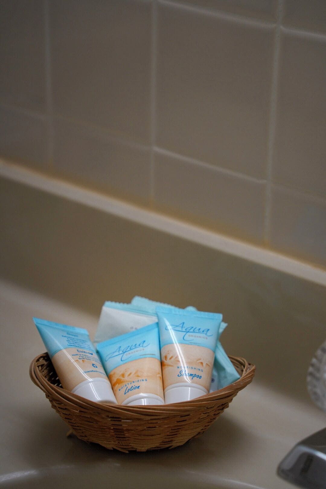 A wicker basket containing several toiletry items, including a moisturizing lotion and shampoo, placed on a bathroom counter.