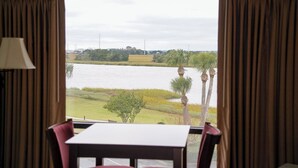A room with a large window overlooking a body of water, a table, and chairs. - Epworth By The Sea (St. Simons Island)