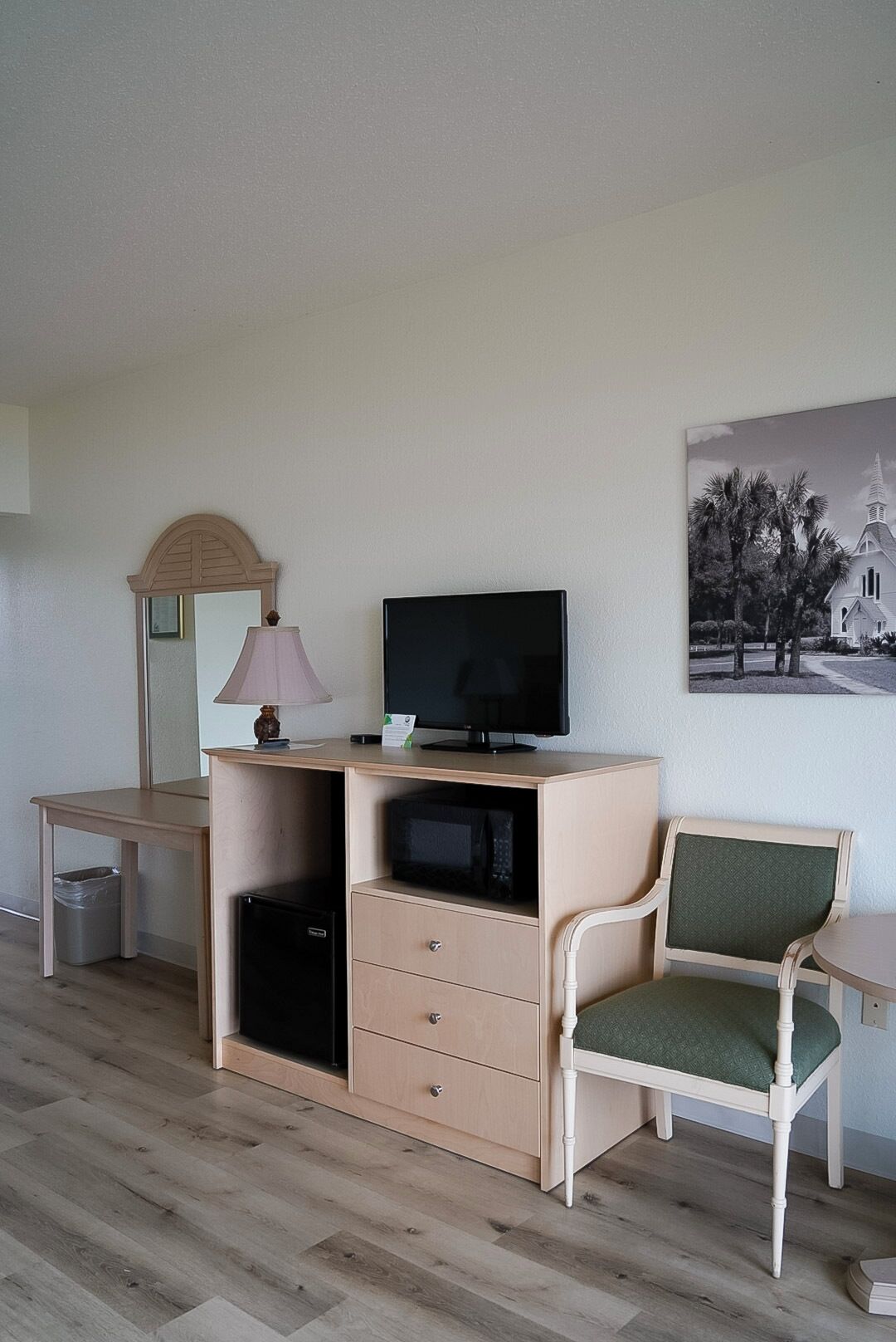 Et værelse med et skrivebord, et fjernsyn, en stol, en lampe og et billede på væggen.