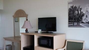 Et værelse med et skrivebord, et fjernsyn, en stol, en lampe og et billede på væggen.