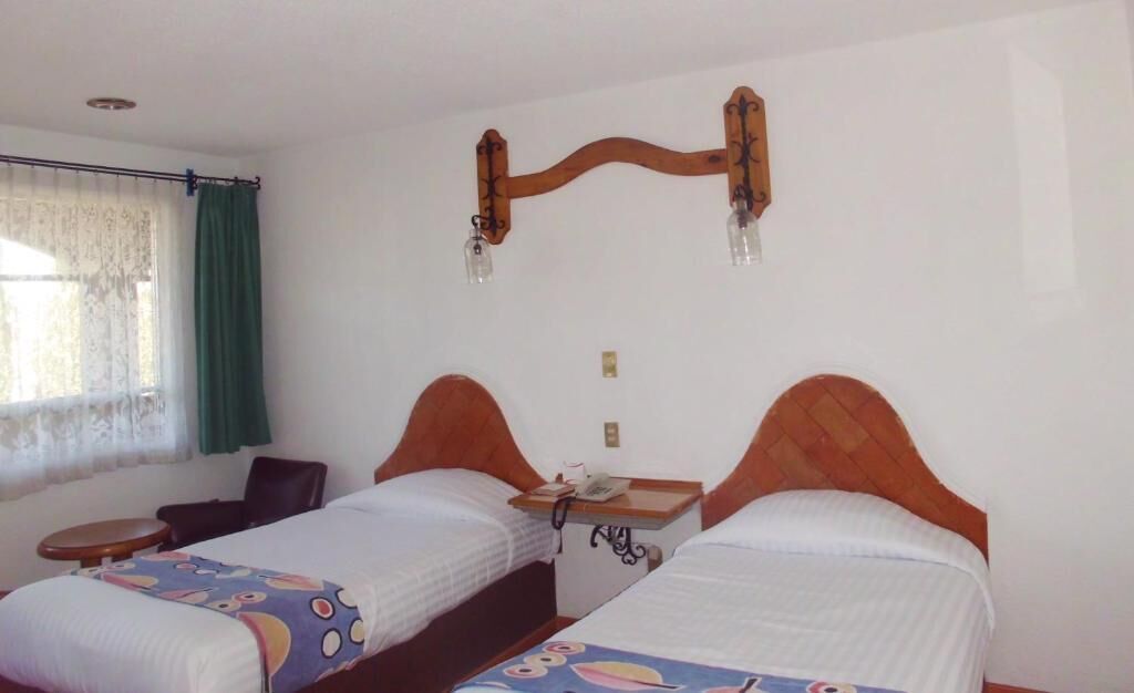 Une chambre avec deux lits simples, une petite table, une chaise et une fenêtre avec des rideaux.