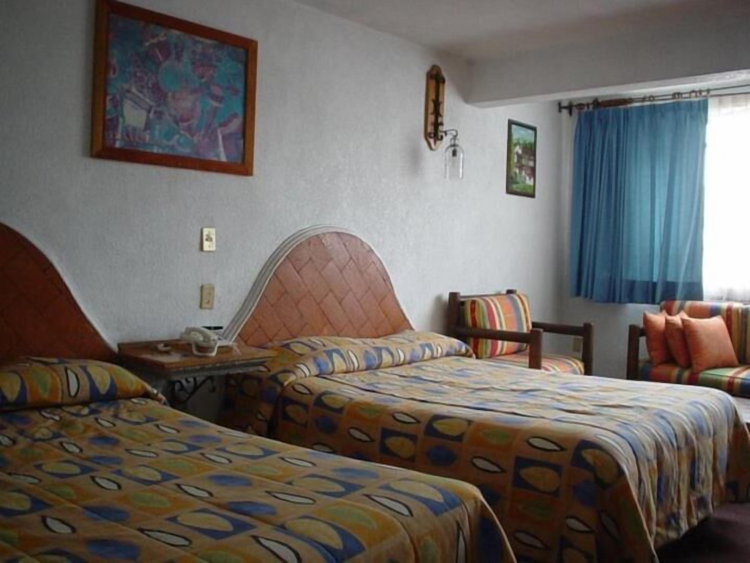 A room with two beds, a chair, a table, and a window with curtains.