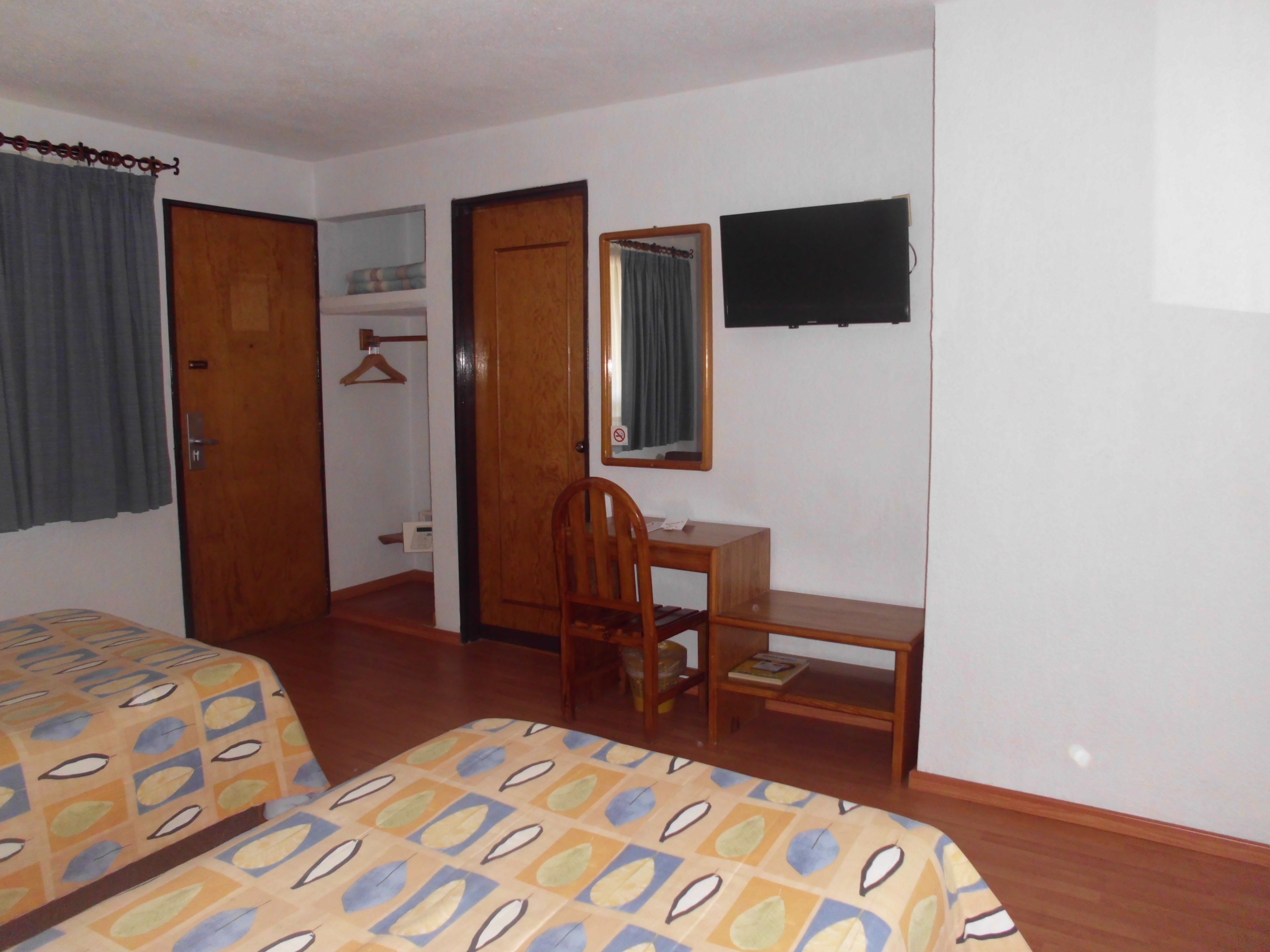 A bedroom with two beds, a desk, a chair, a mirror, and a TV.