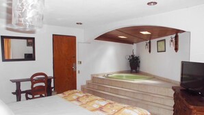 Quarto de hotel com cama, escrivaninha, cadeira, televisão, banheiro com banheira e escada.