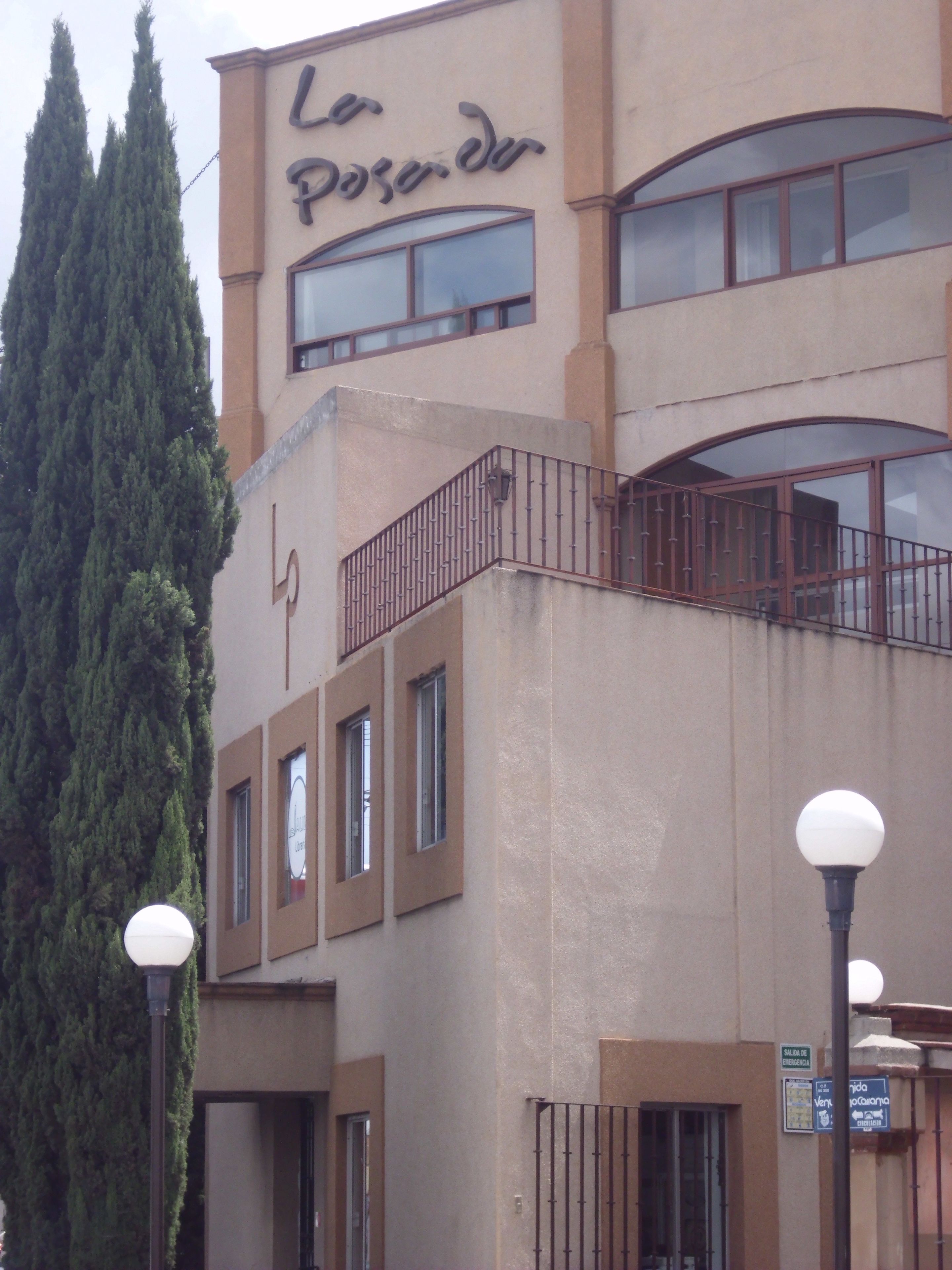 Un edificio con un letrero que dice "La Posadera" y un árbol alto en primer plano.