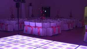 Uma sala de banquetes com mesas redondas, toalhas brancas e cadeiras adornadas com fitas cor-de-rosa.