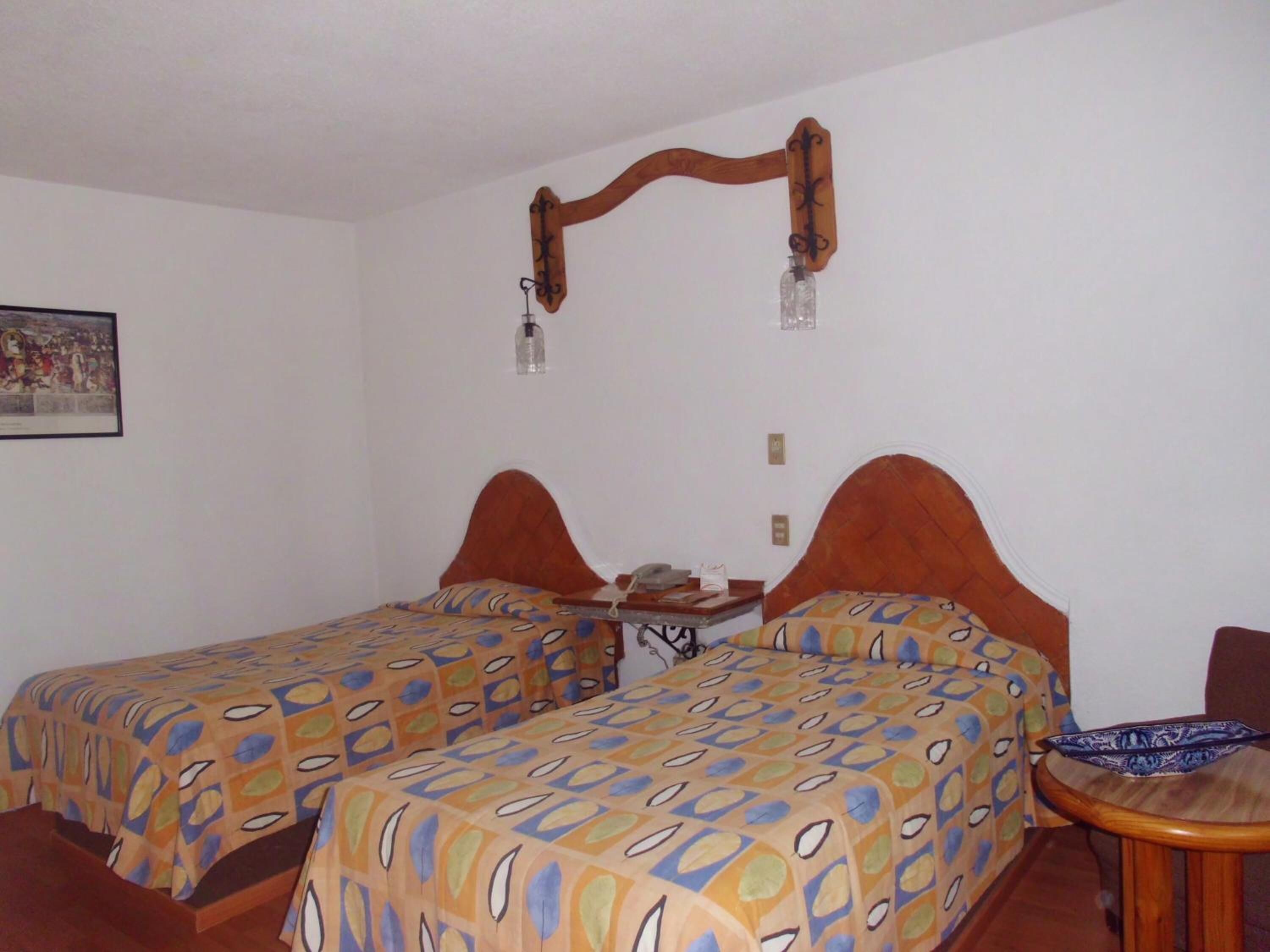 Ein Zimmer mit zwei Betten, jeweils mit einem gemusterten Bettüberwurf, einem Holz-Kopfteil, einem kleinen Tisch mit Telefon und einer wandmontierten Leuchte.