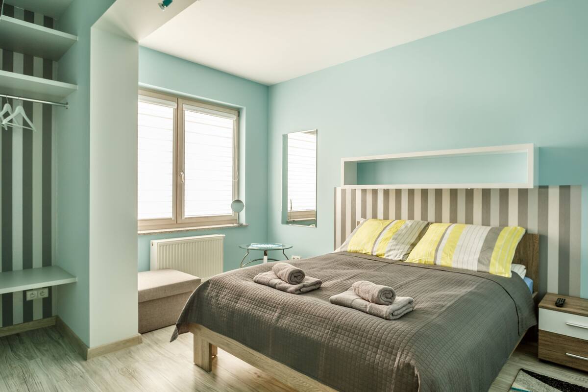 Ein Schlafzimmer mit Bett, Nachttisch, Kleiderschrank und einem Fenster mit Jalousien.