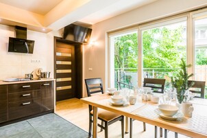 Una cocina moderna con zona de comedor, que cuenta con un amplio ventanal con vistas a la vegetación, una estufa integrada y una mesa de comedor con vajilla y vasos blancos.
