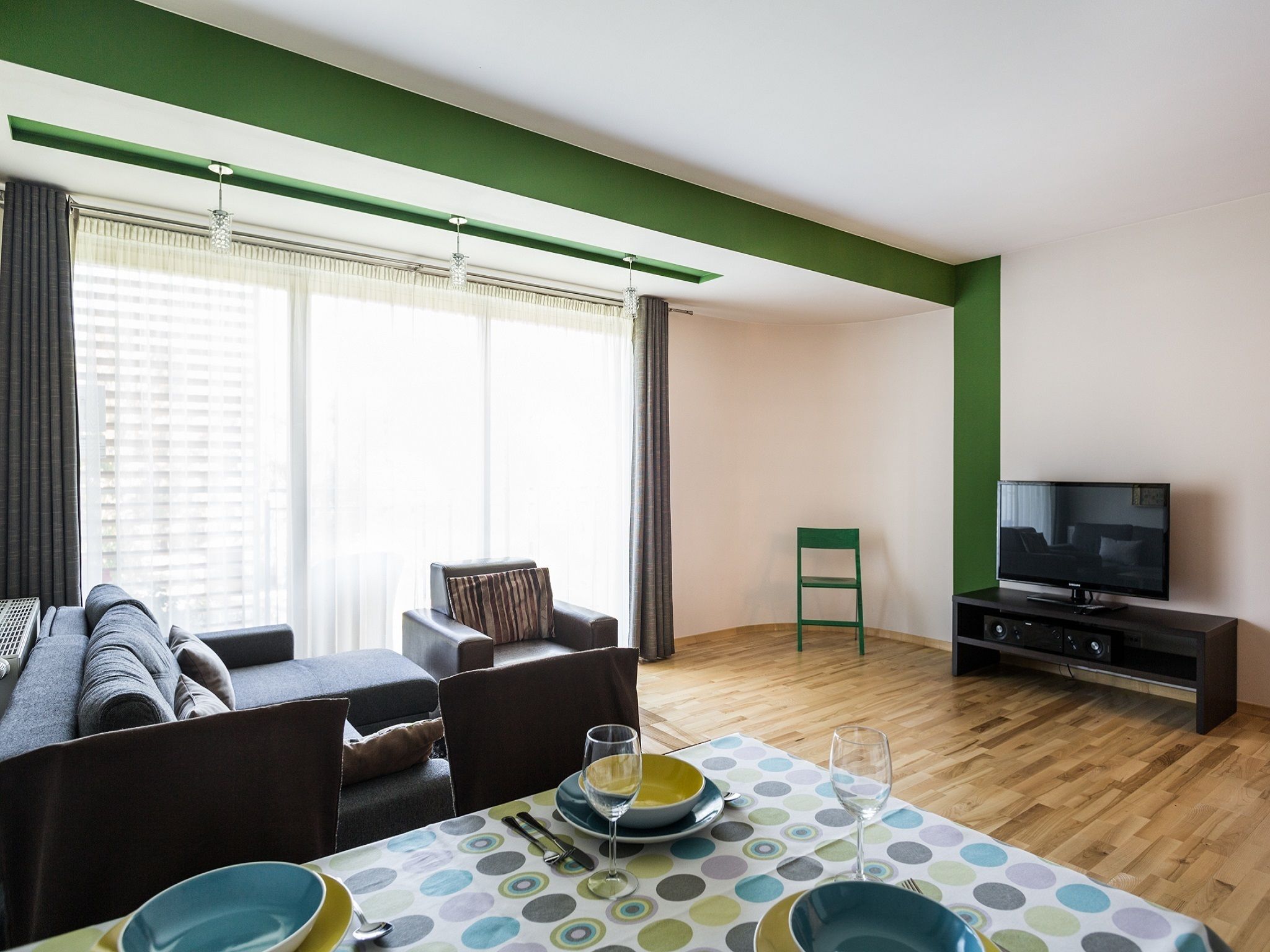 Ein modernes Wohnzimmer mit Essbereich, Fernseher und einer Wand in Grünton.
