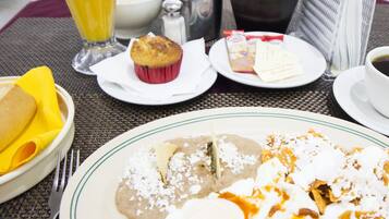 Una escena de desayuno con un plato de enchiladas, un muffin y un vaso de jugo de naranja.