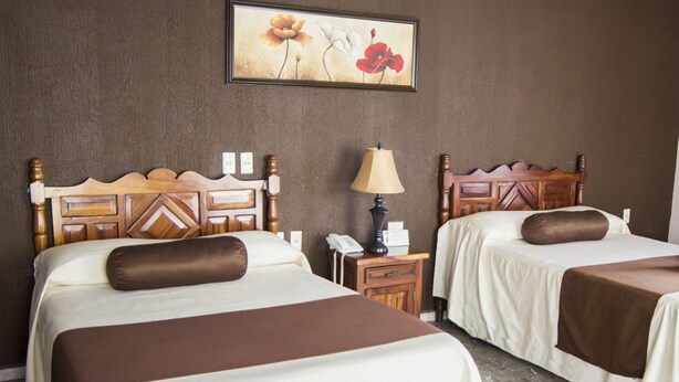 A hotel room with two beds, a nightstand, a lamp, and a painting on the wall. - Hotel San Jorge (Tepic)