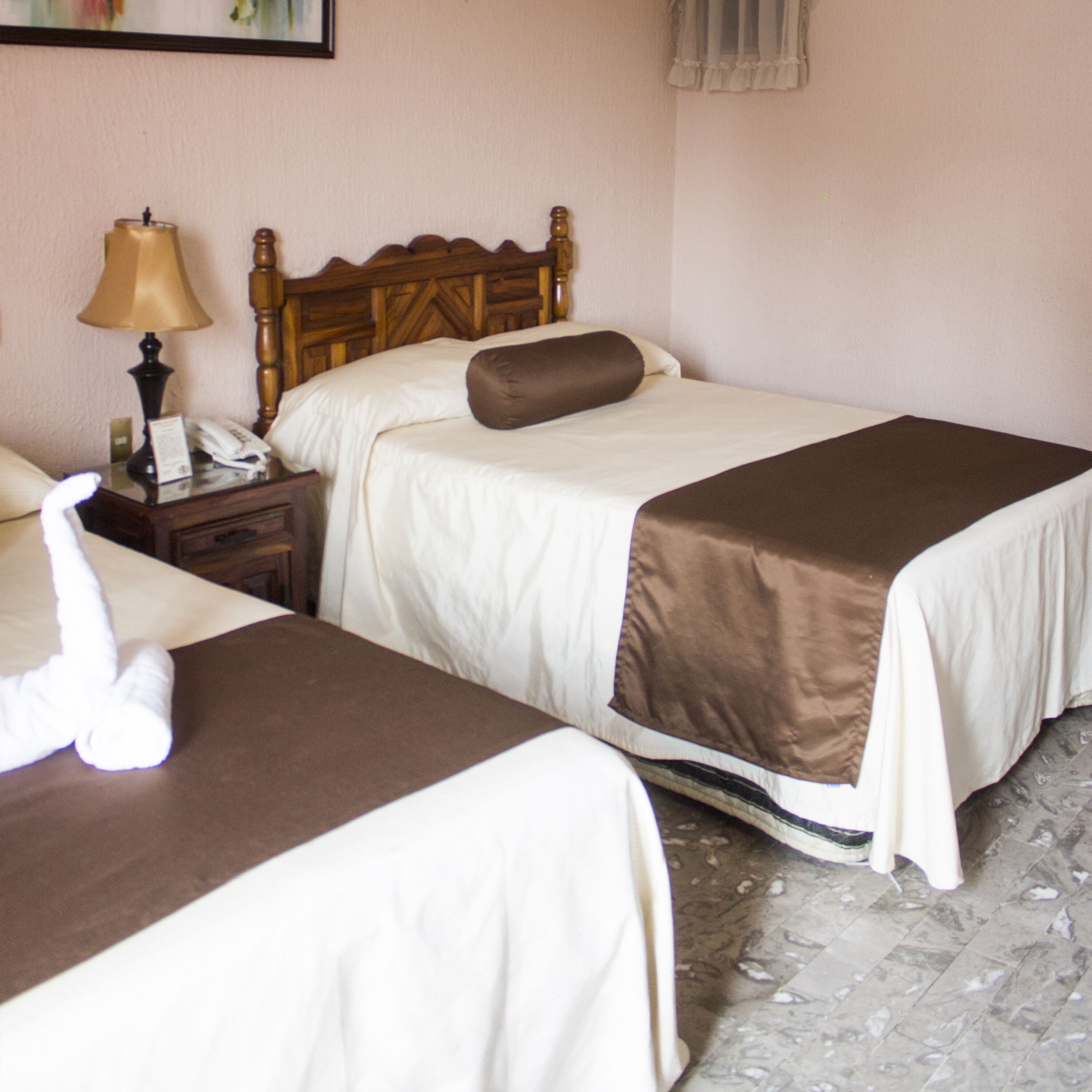 A hotel room with two beds, a nightstand with a lamp, a telephone, and a towel on the floor.