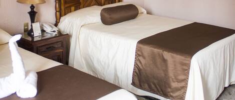 A hotel room with two beds, a nightstand with a lamp, a telephone, and a towel on the floor.