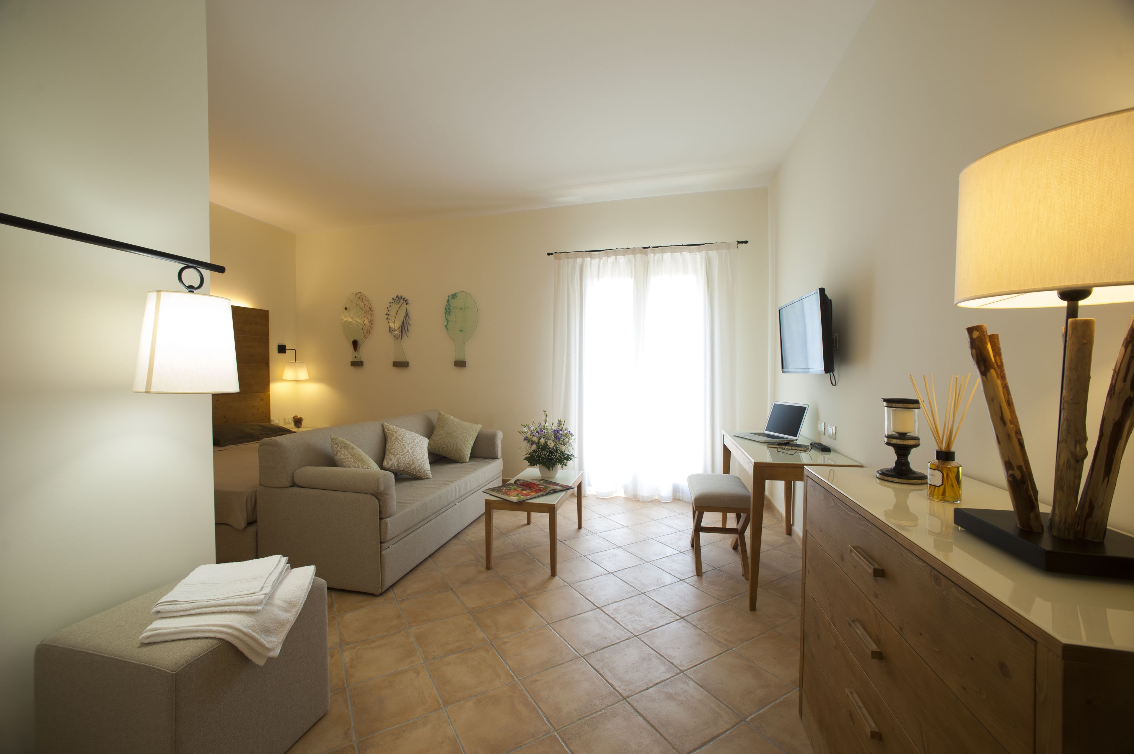 Una sala de estar con sofá, mesa de centro y televisor. Hay un escritorio con silla y lámpara.
