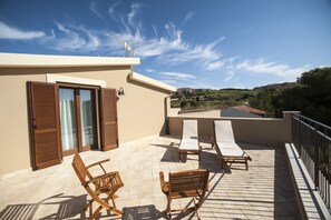A terrace with wooden chairs and a table, a sliding glass door, and a view of the countryside. - Feudo del Biviere (Santa Ninfa)