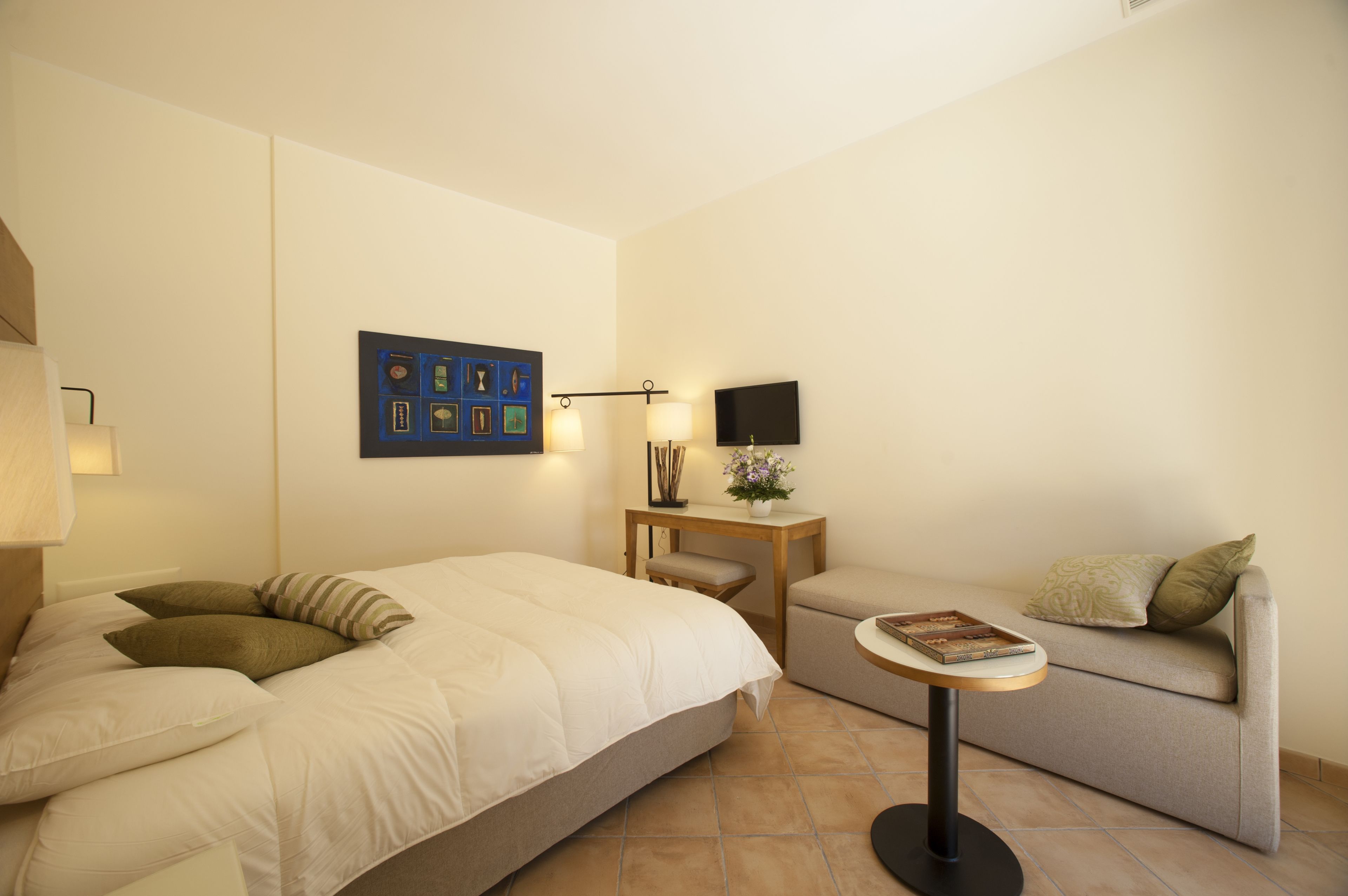 A hotel room with a bed, a sofa, a small table with a lamp, and a wall-mounted TV.