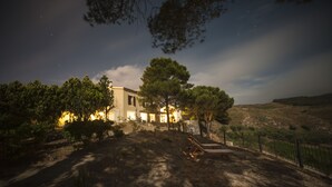 Una casa rústica con un gran árbol en frente, rodeada por un jardín vallado.