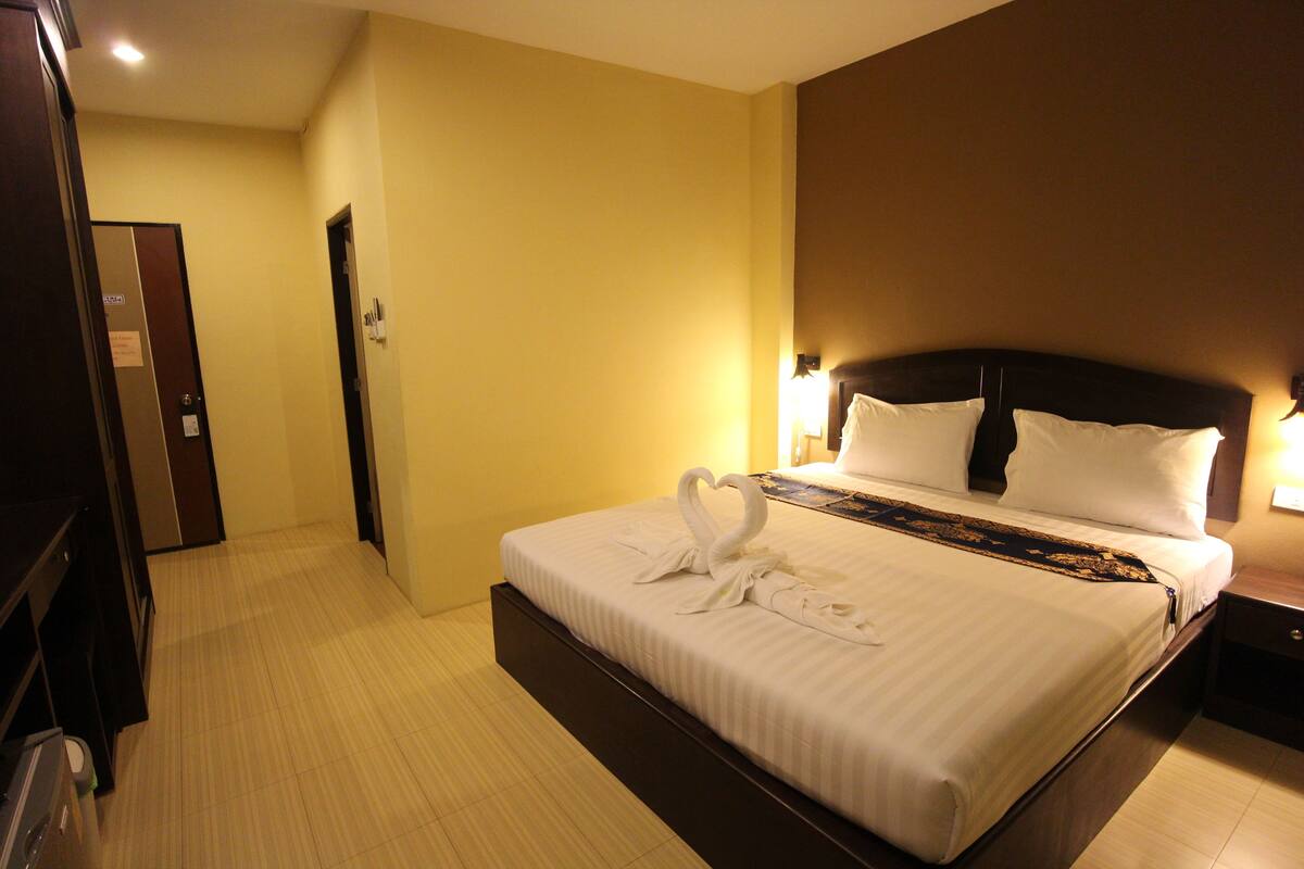 Quarto de hotel com uma cama grande, cabeceira de madeira e mesa de cabeceira com abajur.