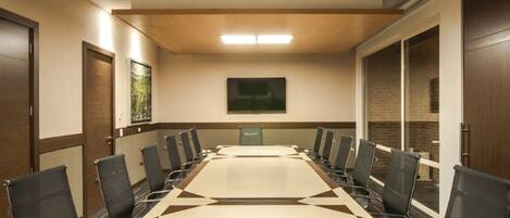 A conference room with a long table, black chairs, wooden paneling, and a framed picture on the wall.