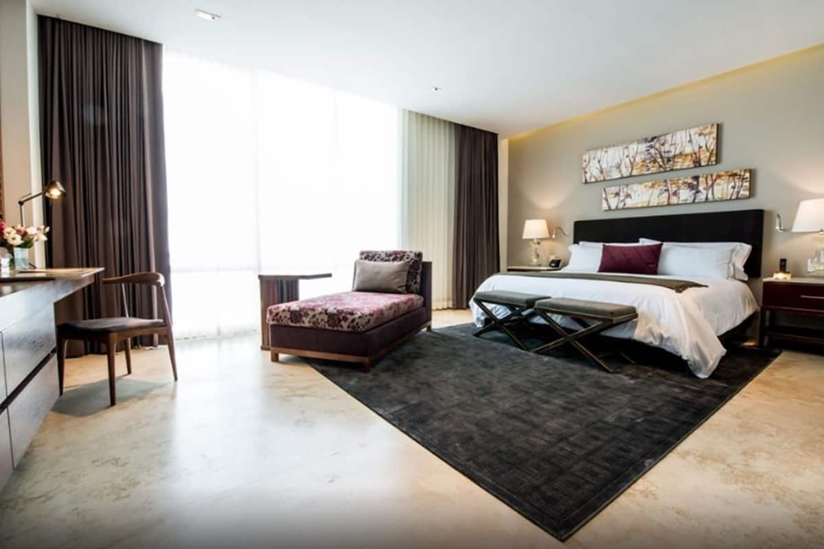 A hotel room with a bed, a desk, a chair, a small table, and a large window.