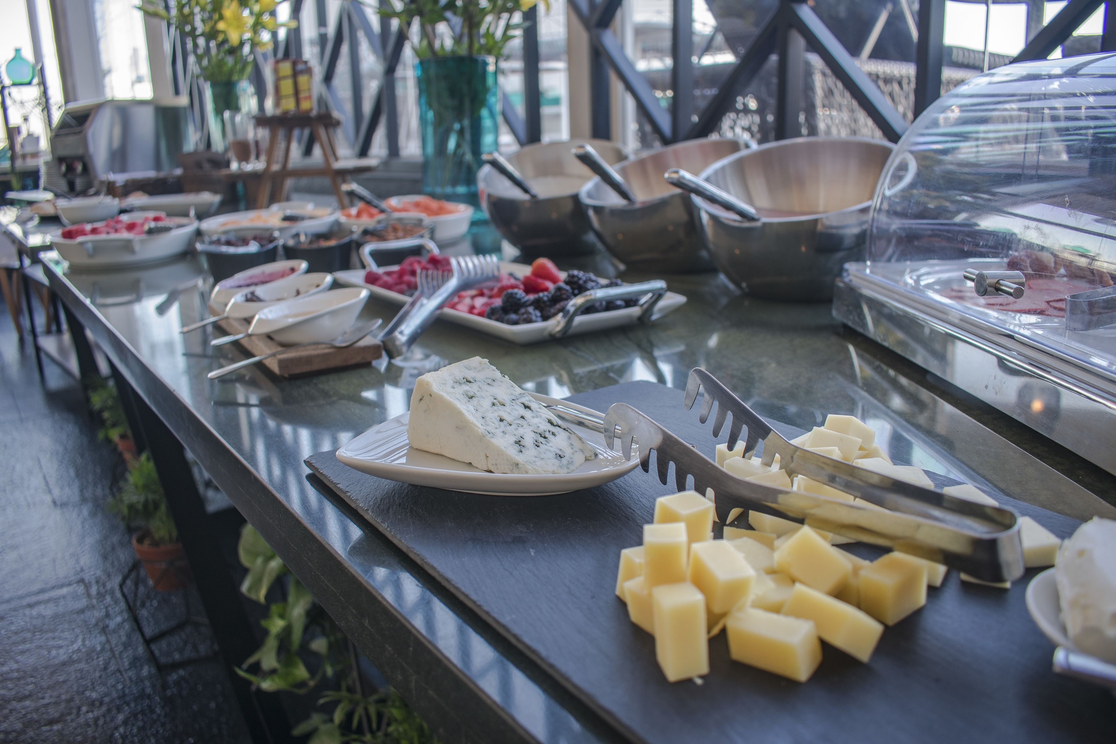 A buffet table with various food items including cheese, fruits, and utensils.