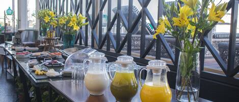 Una mesa de buffet con diversos alimentos y tres jarras de bebidas de diferentes colores.