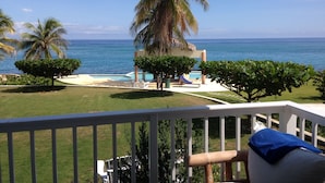A balcony with a view of the ocean, a pool area, and palm trees. - Whispering Seas (Tower Isle)