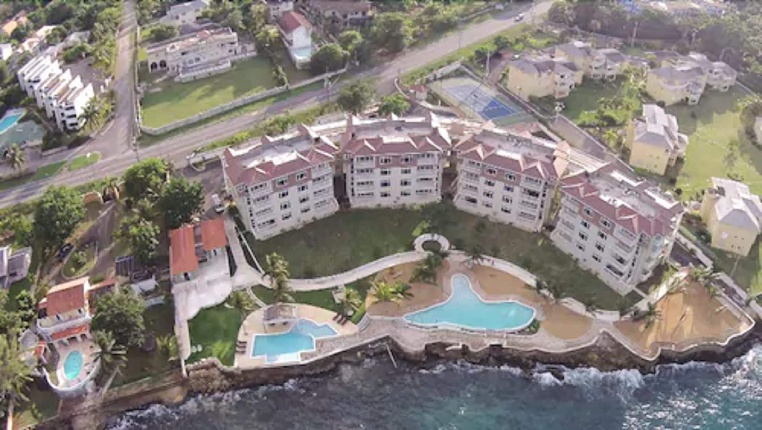 A coastal hotel with multiple buildings, a central swimming pool, and a smaller adjacent pool.