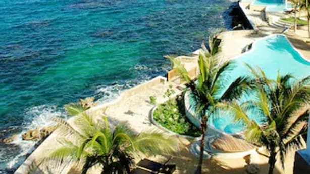 A coastal resort with a clear view of the ocean, a swimming pool, and a sandy beach area. - Whispering Seas (Tower Isle)