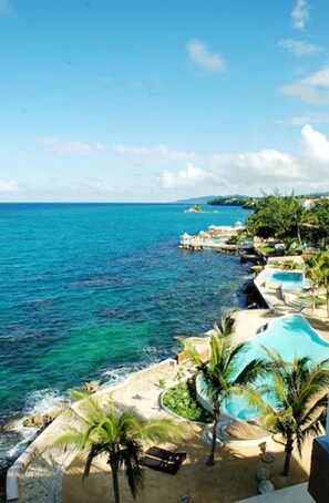 A coastal resort with a clear view of the ocean, a swimming pool, and a sandy beach area.